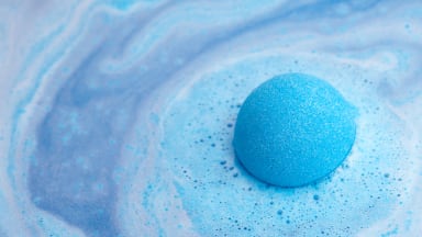A blue bath bomb starts to foam turning the water around it different shades of blue.