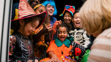 Happy children in different festive Halloween costumes at door collecting candy from bowl.