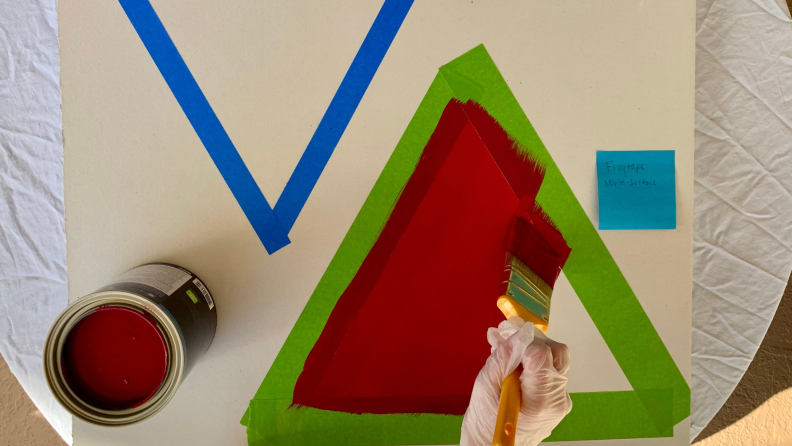 一个人用油漆刷和红色内饰漆在干墙板上画绿色油漆工胶带的内线