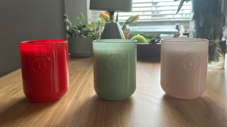 The three different Glossier candles lined up in a row on a table.
