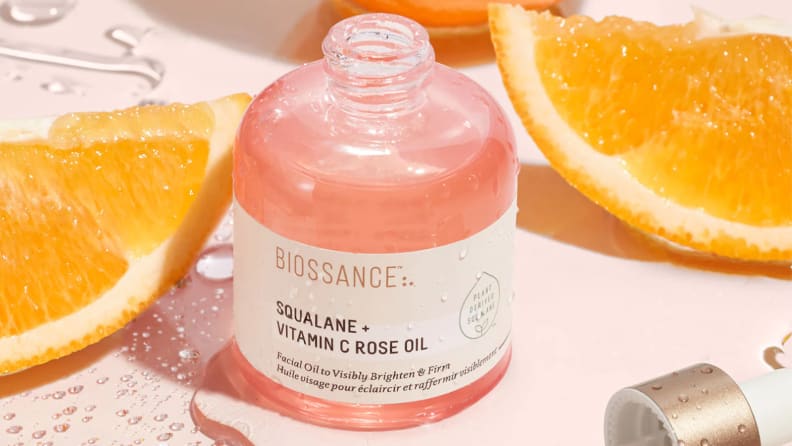 A clear bottle full of light pink liquid on a light pink background with orange slices around it.
