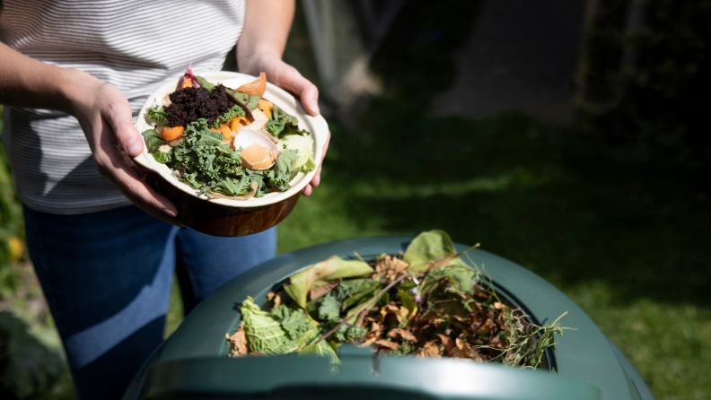 A person adds organic greens to a compost pile.