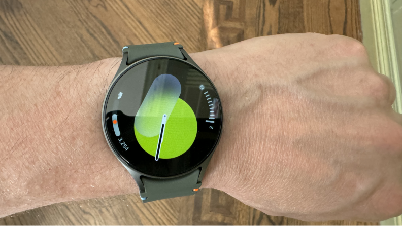 A wrist wearing the smartwatch displaying a green screen.