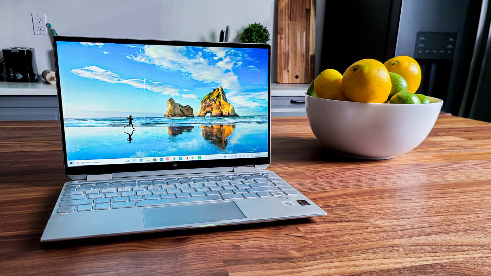 An HP Spectre laptop sitting next to a bowl of fake fruit.