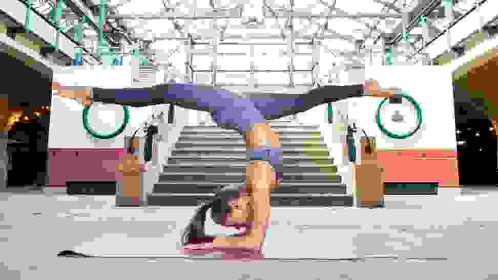 An athlete strikes a balanced headstand pose on a yoga mat.
