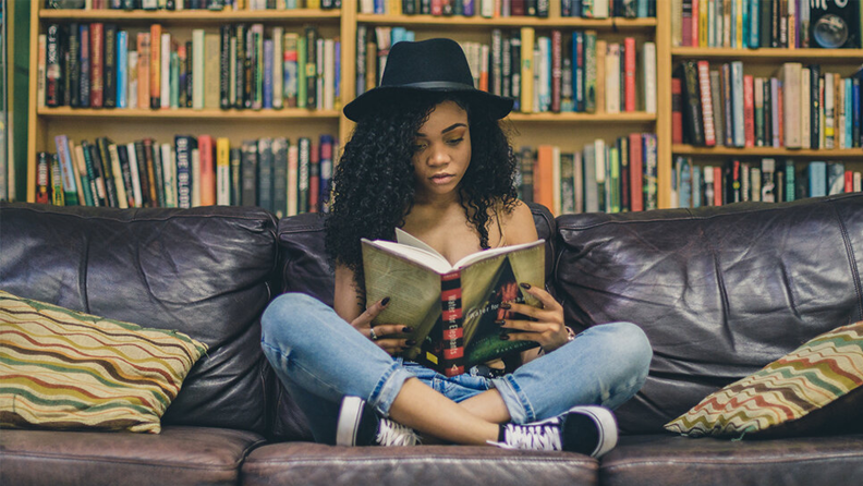 A woman reads on a couch in front of shelves of books