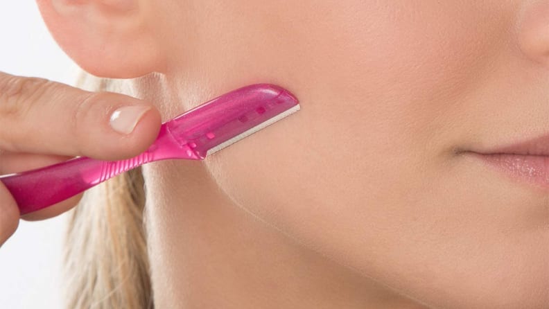 A closeup of a woman holding a dermaplane tool on her jawline pointing downward.