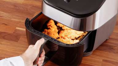 Person resting their hand on the handle of the basket of an air fryer that has fried chicken inside.