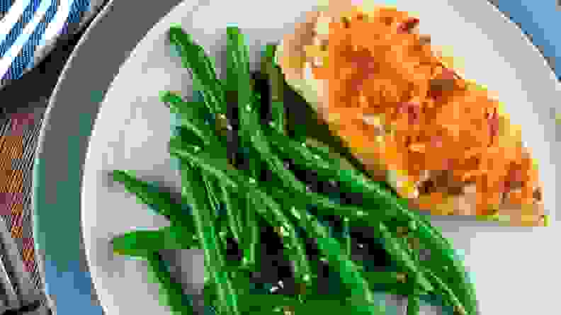 A top-down photo of a plate filled with a chicken breast and green beans.