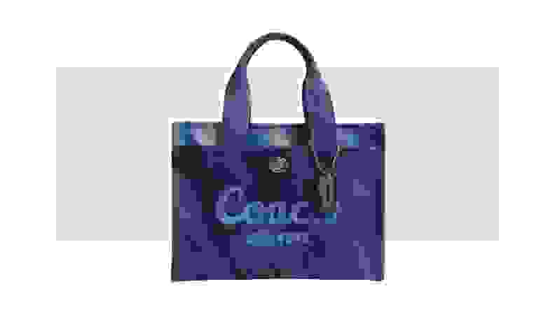 A canvas tote bag in blue tie-dye fabric, with the Coach logo across the front.