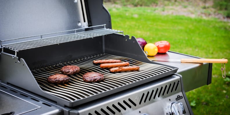 Gas grill open, revealing cooking burgers and hot dogs