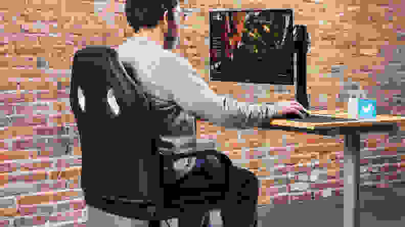 A person sitting on the Amazon Basics Racing/Gaming style office chair using a computer on a monitor.