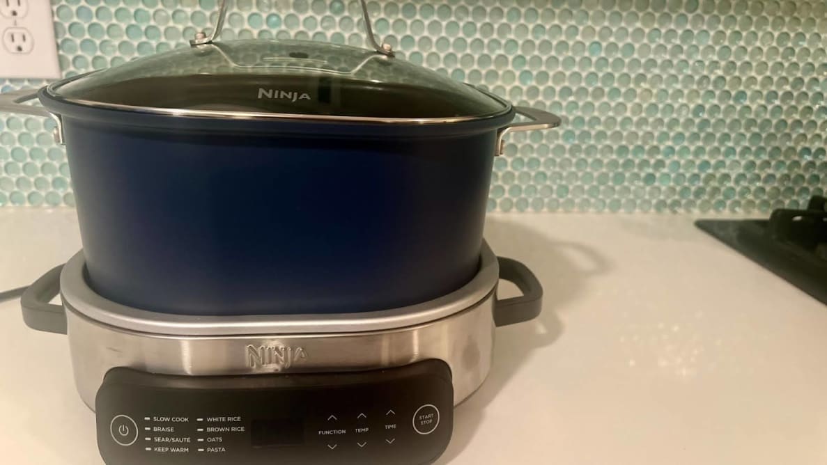The Ninja Foodi PossibleCooker Slow Cooker on a marble countertop next to stove in front of teal backsplash.