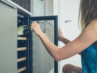 A woman pulls a bottle of wine out of a wine refrigerator.