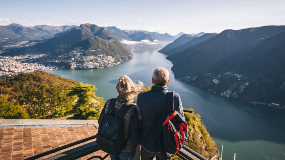 Two people stand on a cliff and look out at a lake.