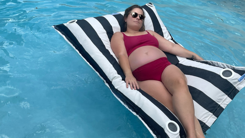 Person in red swimsuit and sunglasses lounges on top black and white pool lounger in water.