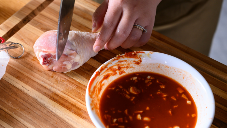 A hand scoring a chicken leg on a cutting board