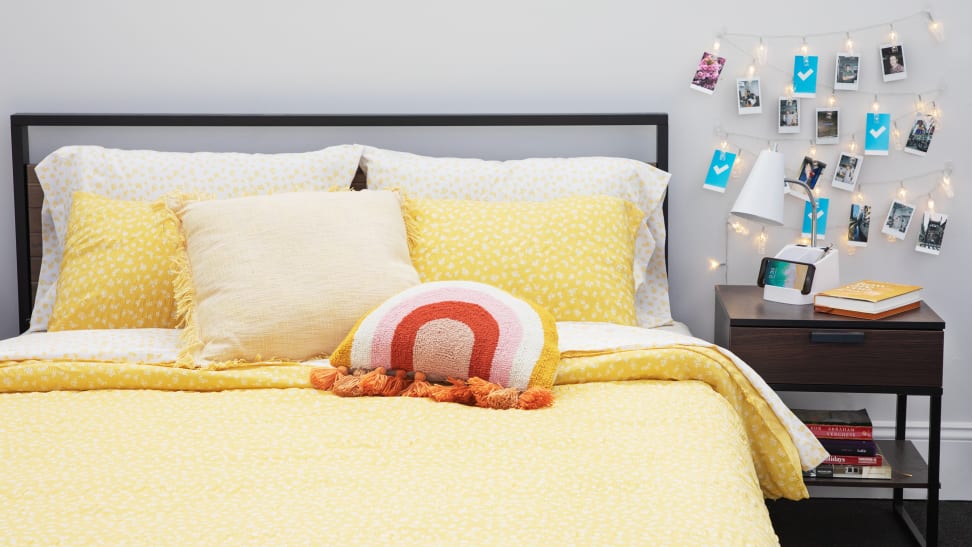 A dorm room with a yellow comforter on a bed, string lights, and polaroid photos on display.