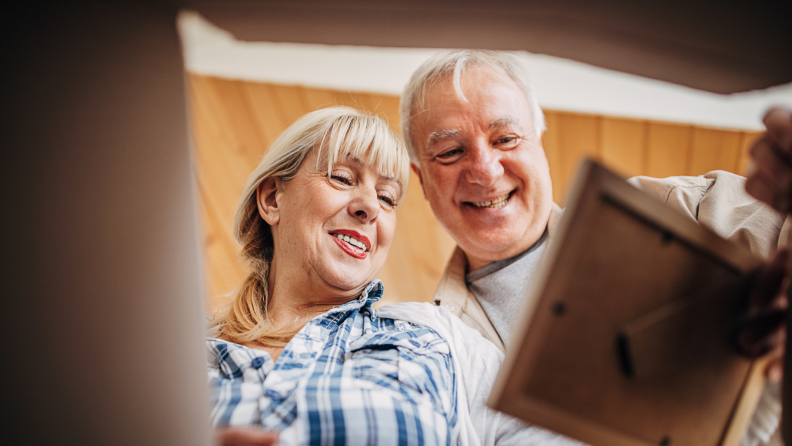 Senior couple smiling at picture frame before placing it in box.