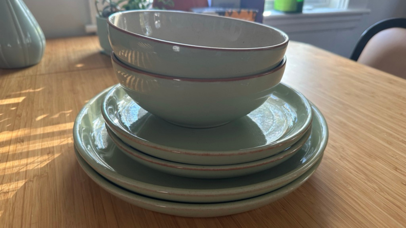 A stack of Denby with two cereal bowls, two salad plates, and two dinner plates on a dining table.