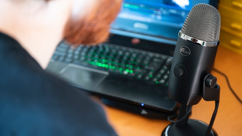A man with a red beard speaks into a Blue Yeti X USB microphone that's sitting on a desk.