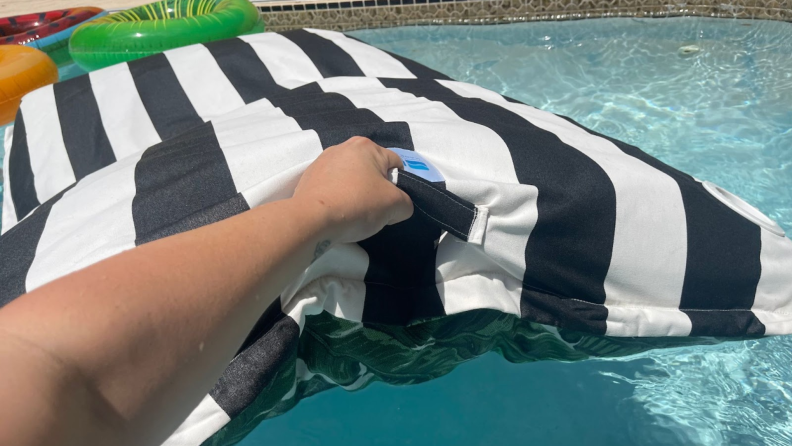 A hand holding on to the handle of the Laze Pillow in a pool and lifting it out of the water.