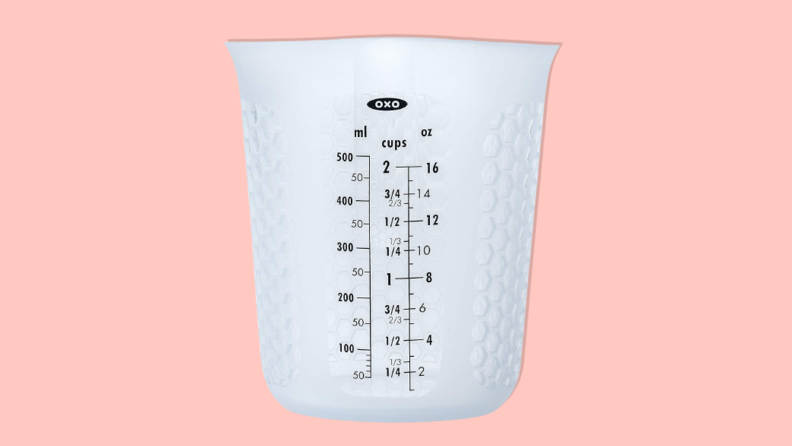 OXO Good Grips 2-cup Squeeze and Pour Silicone Measuring Cup on a pink background.