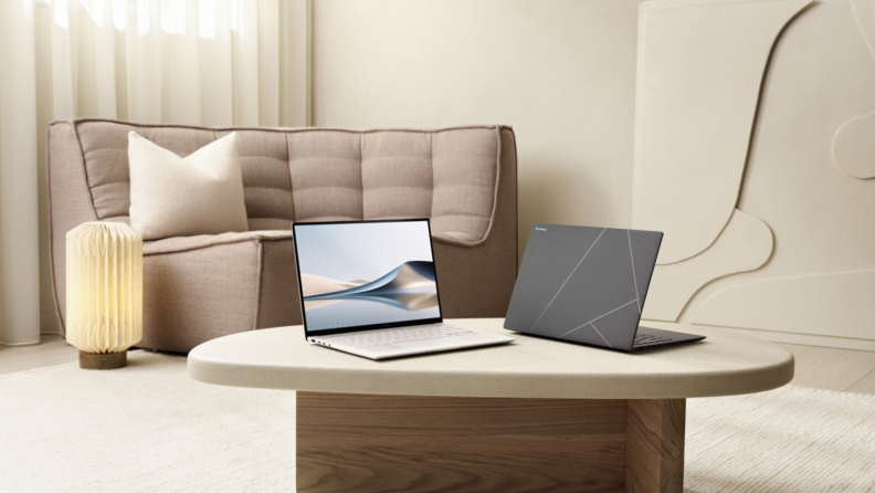 Two Asus Zenbook S 14 laptops on the coffee table of a neutral-colored minimalist living room with sofa and paper lantern.