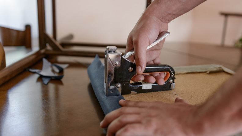 Person using staple gun to attach fabric to wooden board.