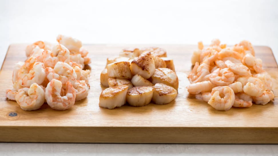 Shrimp and scallops sitting on a wooden cutting board.
