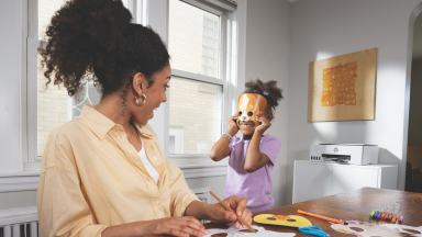 A mom and daughter smile while crafting animal masks at home, with an HP printer in the background.