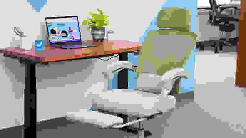 Green Ergonomic Office Chair with footrest extended, positioned in front of desk with laptop computer .