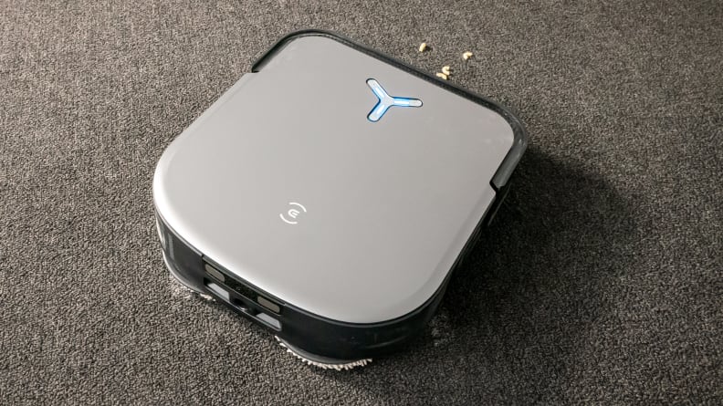 A square, gray robot vacuum stands on  gray carpet