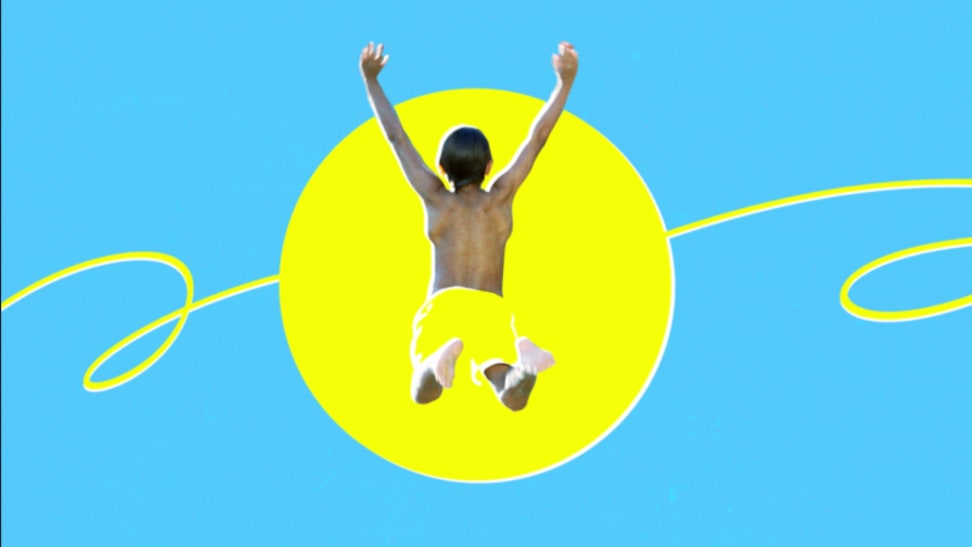 A boy jumps into the sun wearing yellow swim trunks