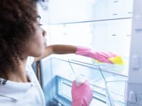A person wearing rubber gloves wipes down the shelves in a fridge with a cloth