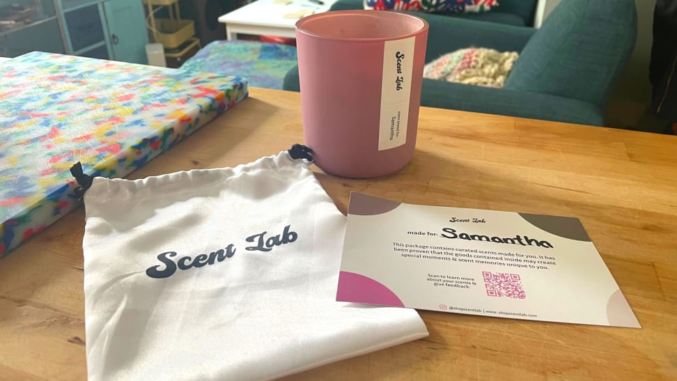 A pink Scent Lab candle displayed on a wood table with a Scent Lab bag and product information card