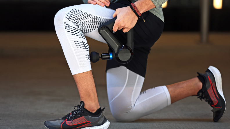 A man massaging his legs with a Theragun massage gun.