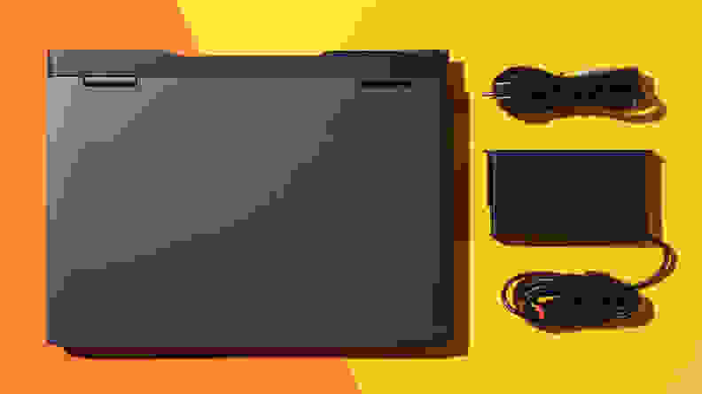 The Lenovo IdeaPad Gaming 3 laptop next to USB cords and charger, on an orange background.