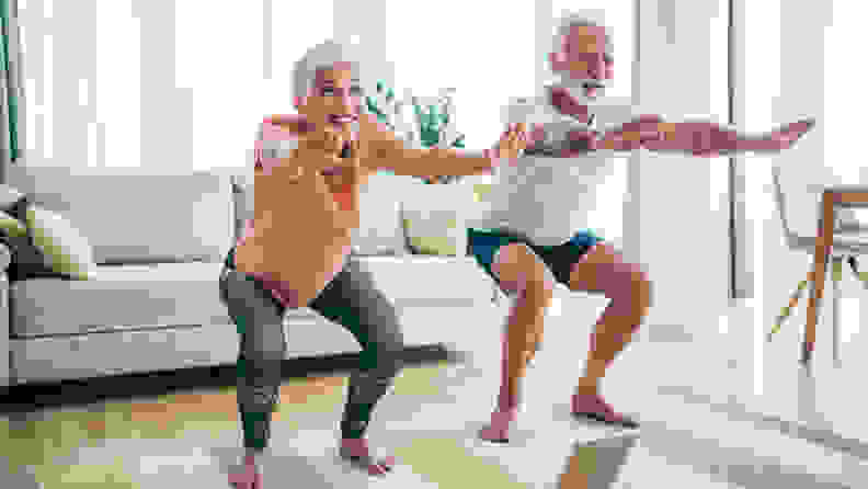 An elderly man and woman stand side by side with arms outstretched in a yoga pose