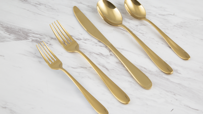 Golden flatware (knives, forks, spoons) sit together on a marble countertop.