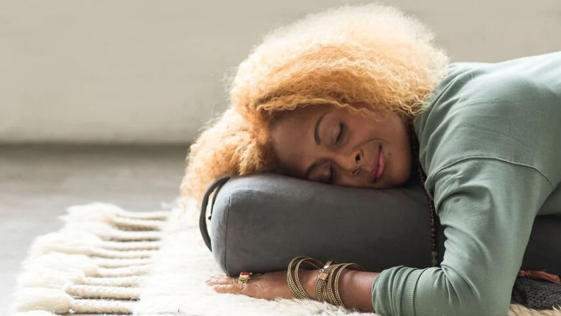 A woman laying on a Manduka Enlight Rectangular Bolster on the ground.