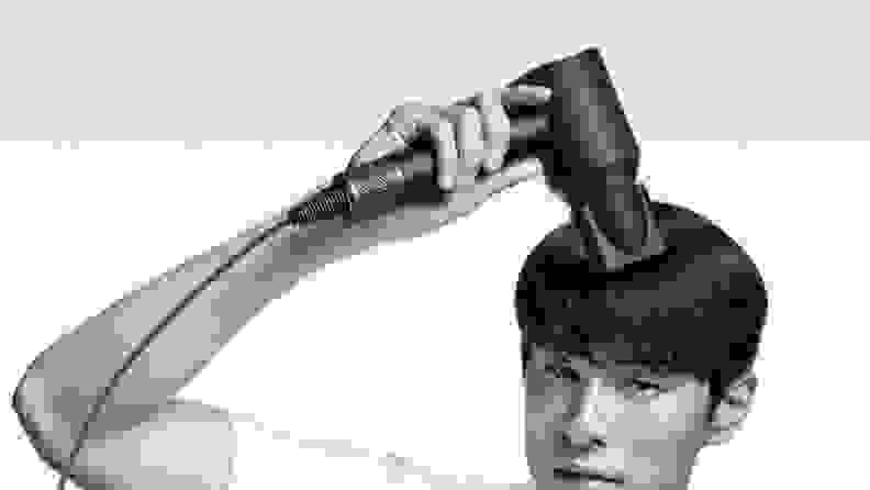 A person using the Dyson Supersonic hair dryer in front of a blank background.