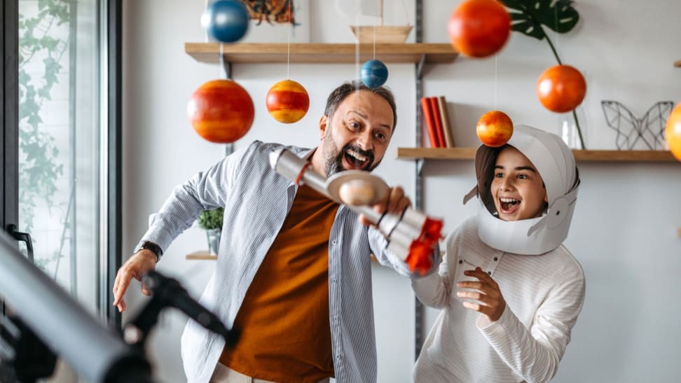 Little girl and dad playing with her homemade planetarium as she holds a rocket ship while laughing.