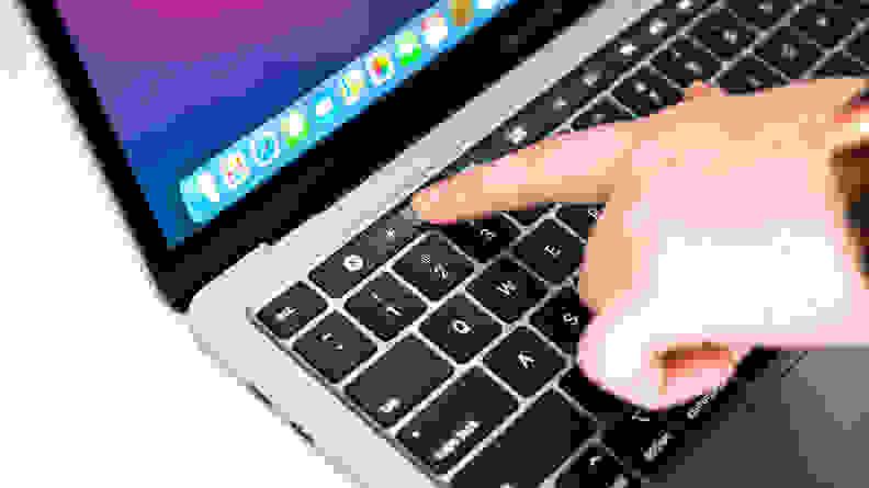 Close-up: A fingertip presses the brightness control on a MacBook Pro's touchscreen toolbar (at the top of the keyboard).