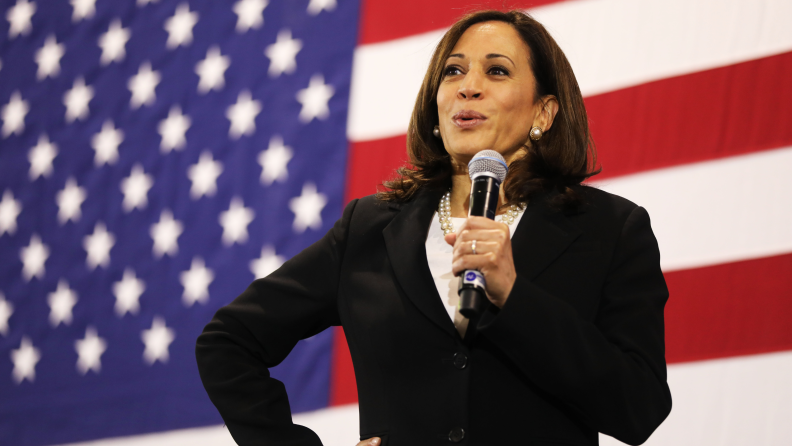 An image of Vice President Kamala Harris wearing a pearl necklace and standing in front of the US Flag.