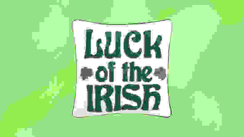 A white pillow with Luck of the Irish stiched on in front of a green background.