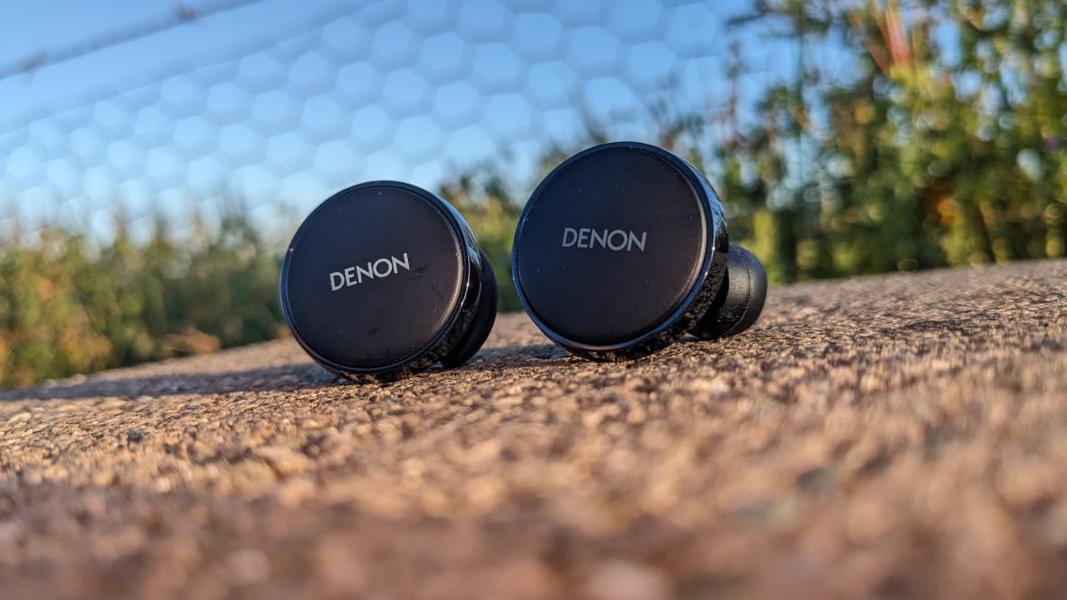 A pair of Denon PerL Pro earbuds on top of cement outdoors.