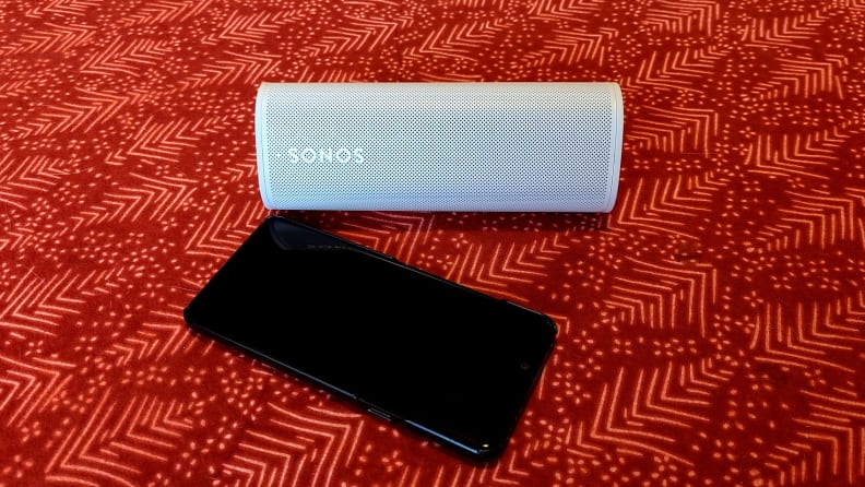 The white and tubular Sonos Roam on red table top next to a phone