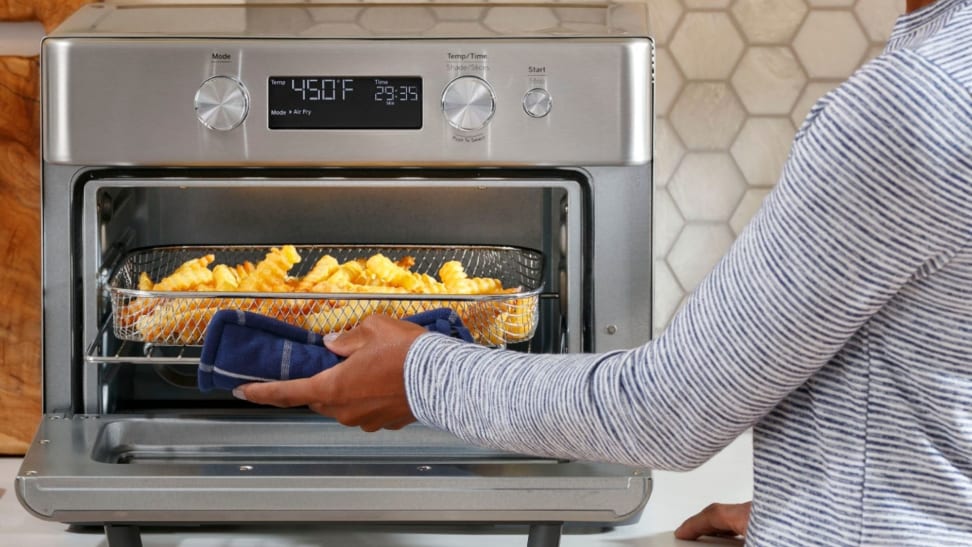 A woman removes a pan of French fries from GE's 8-in-1 Air Fryer Toaster Oven.