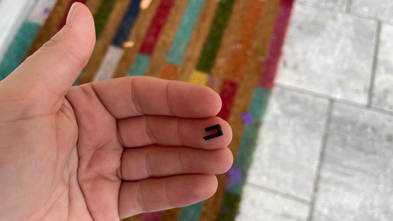 A hand holding a broken plastic piece of a video doorbell.